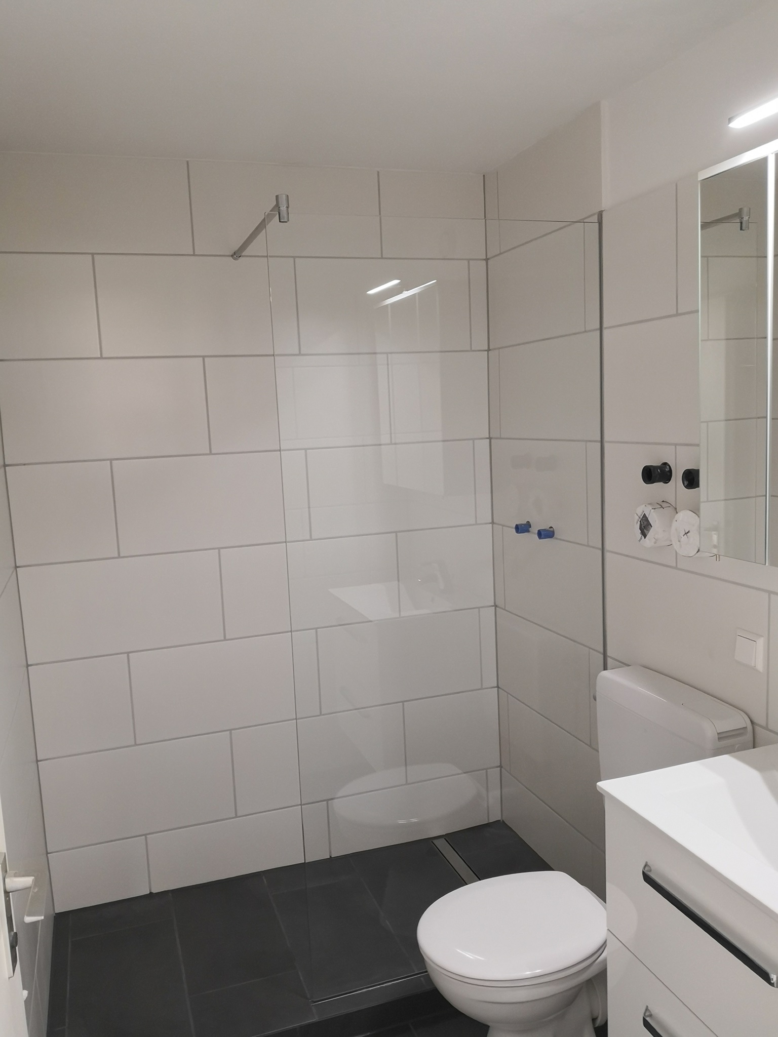 Weiß gefliestes Bad mit Glasdusche und dunklem Boden